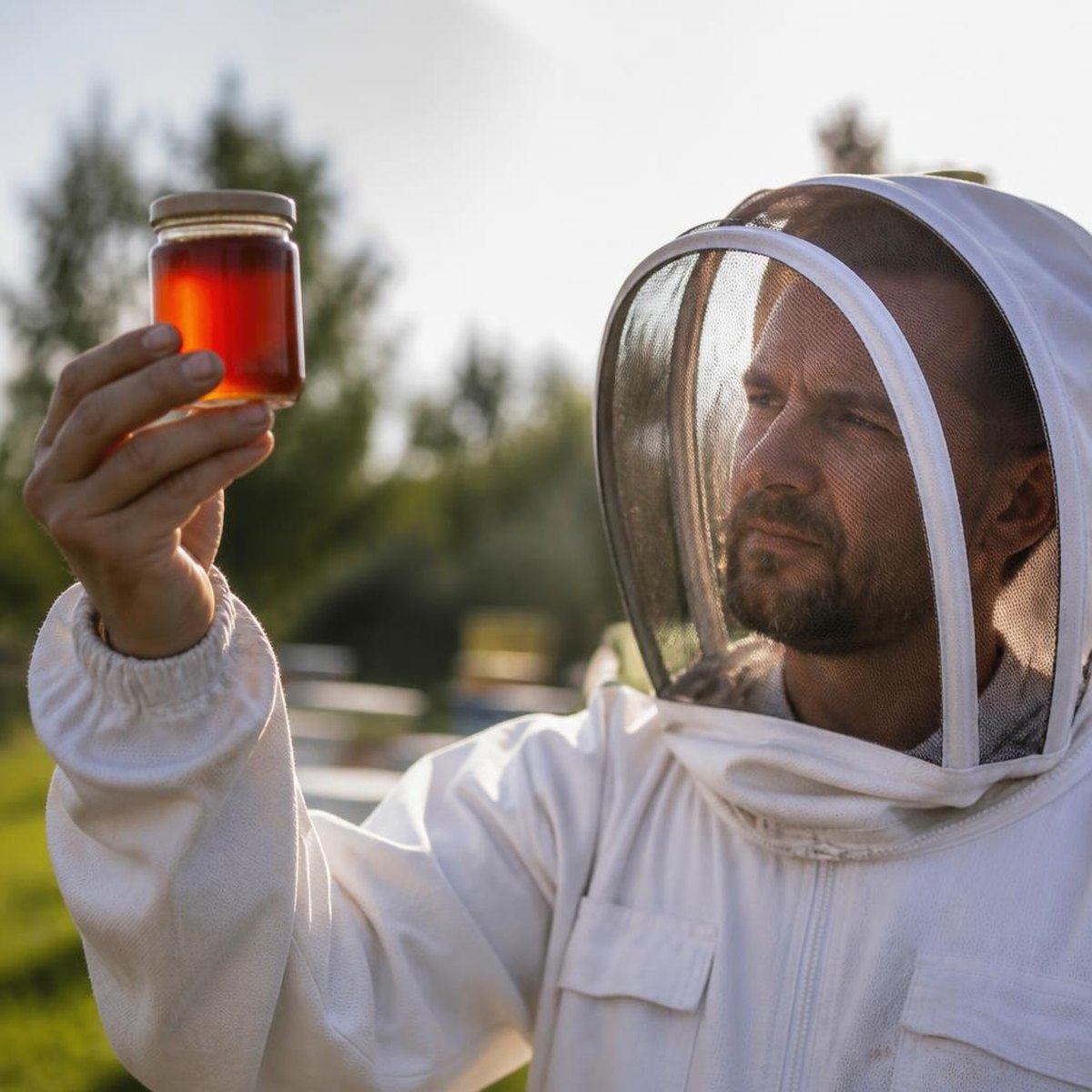 Beekeeper In A White Suit Holding A Jar Of Dark Amber